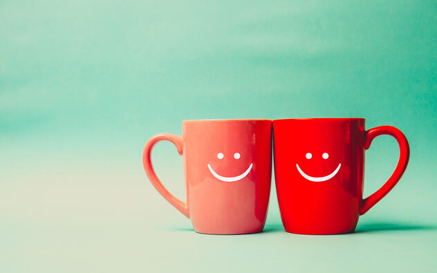 2 rode koffiekoppen tegen elkaar, met daarop een lachend gezichtje