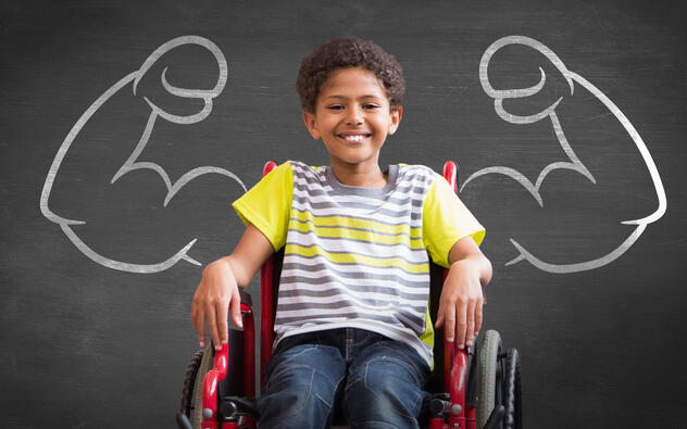 jongen in rolstoel voor een schoolbord waarop sterke armen met spierballen getekend zijn